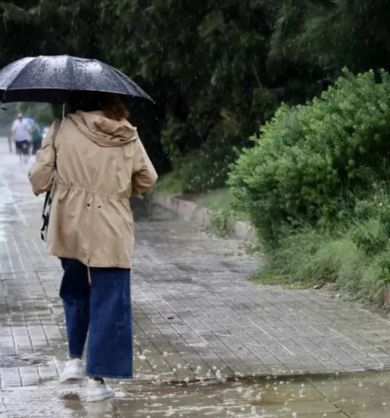 Άτομο με ομπρέλα και αδιάβροχο περπατά σε βρεγμένο πεζοδρόμιο υπό βροχή