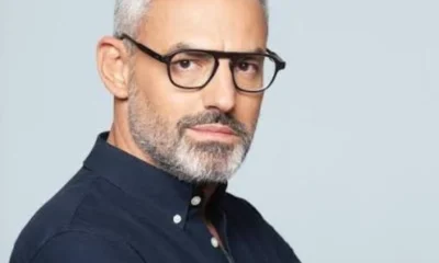 Άντρας με γυαλιά οράσεως, γκρίζα μαλλιά και μούσι φοράει σκούρο πουκάμισο σε ανοιχτόχρωμο φόντο