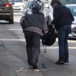 Δύο άτομα στεκόμενα σε δρόμο ανάμεσα σε σταθμευμένα αυτοκίνητα, με αντικείμενα στο οδόστρωμα.