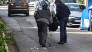 Δύο άτομα στεκόμενα σε δρόμο ανάμεσα σε σταθμευμένα αυτοκίνητα, με αντικείμενα στο οδόστρωμα.