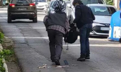 Δύο άτομα στεκόμενα σε δρόμο ανάμεσα σε σταθμευμένα αυτοκίνητα, με αντικείμενα στο οδόστρωμα.