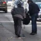 Δύο άτομα στεκόμενα σε δρόμο ανάμεσα σε σταθμευμένα αυτοκίνητα, με αντικείμενα στο οδόστρωμα.
