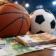 Μπάλα μπάσκετ, μπάλα ποδοσφαίρου και χαρτονομίσματα ευρώ σε ξύλινη επιφάνεια.