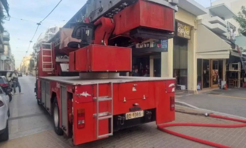 Κόκκινο πυροσβεστικό όχημα σταθμευμένο σε δρόμο μπροστά από καταστήματα