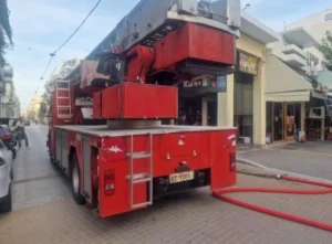 Κόκκινο πυροσβεστικό όχημα σταθμευμένο σε δρόμο μπροστά από καταστήματα