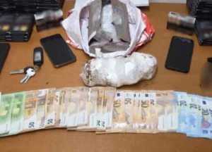 Πάνω σε τραπέζι ακουμπούν χαρτονομίσματα, κινητά τηλέφωνα, κλειδιά και δέματα με πιθανές παράνομες ουσίες.