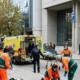 Διασώστες και αστυνομικός σε δρόμο μπροστά από κτήριο με ελληνική σημαία.
