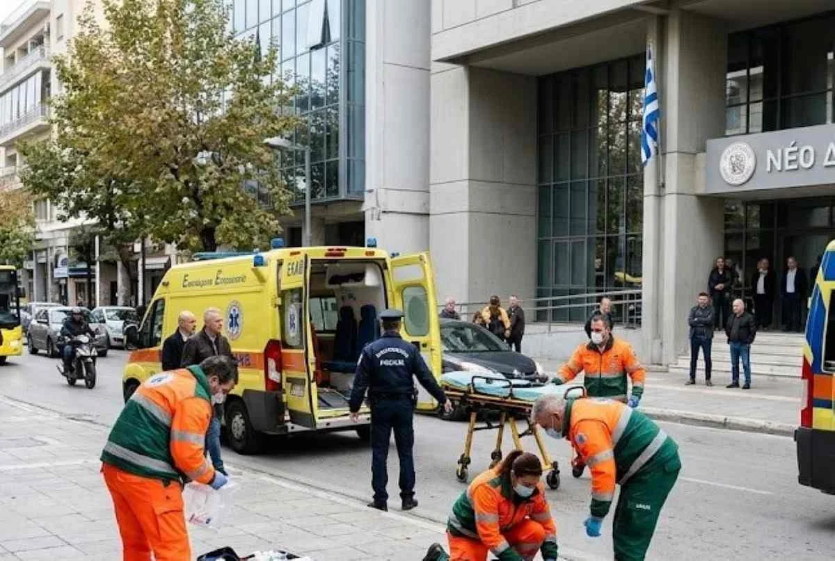 Διασώστες και αστυνομικός σε δρόμο μπροστά από κτήριο με ελληνική σημαία.