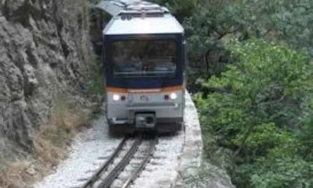 Τρένο κινείται στις γραμμές δίπλα σε βραχώδη πλαγιά και δέντρα