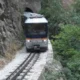 Τρένο κινείται στις γραμμές δίπλα σε βραχώδη πλαγιά και δέντρα
