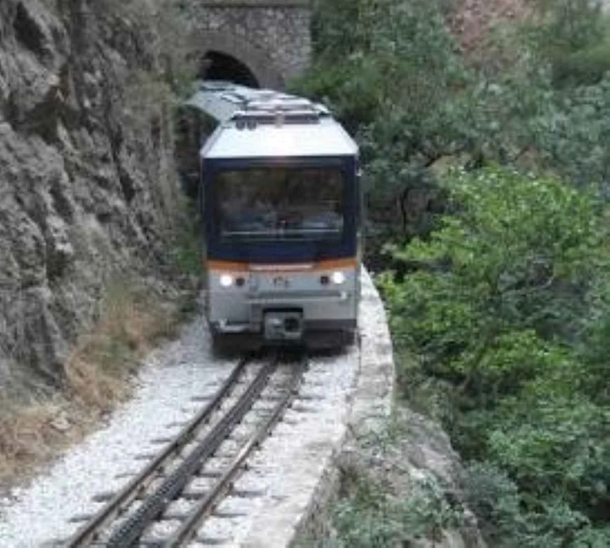 Τρένο κινείται στις γραμμές δίπλα σε βραχώδη πλαγιά και δέντρα