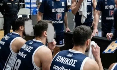 Αθλητές καλαθόσφαισης με μπλε εμφάνιση καθισμένοι στον πάγκο μαζί με προπονητικό προσωπικό σε κλειστό γήπεδο μπάσκετ
