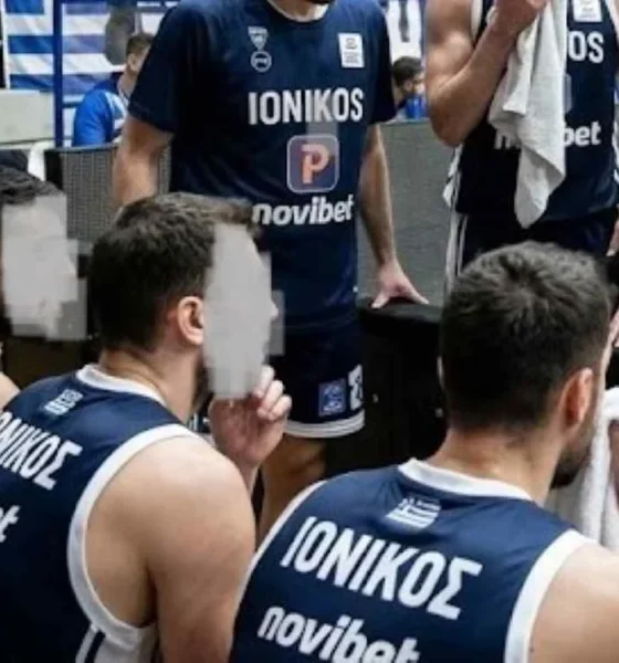 Αθλητές καλαθόσφαισης με μπλε εμφάνιση καθισμένοι στον πάγκο μαζί με προπονητικό προσωπικό σε κλειστό γήπεδο μπάσκετ