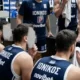 Αθλητές καλαθόσφαισης με μπλε εμφάνιση καθισμένοι στον πάγκο μαζί με προπονητικό προσωπικό σε κλειστό γήπεδο μπάσκετ