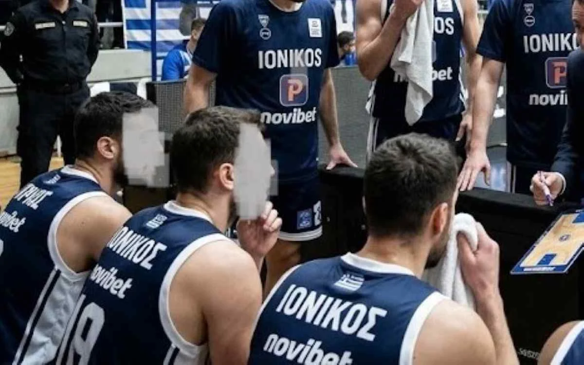 Αθλητές καλαθόσφαισης με μπλε εμφάνιση καθισμένοι στον πάγκο μαζί με προπονητικό προσωπικό σε κλειστό γήπεδο μπάσκετ