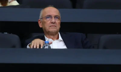 Άντρας με γυαλιά και λευκό πουκάμισο κάθεται σε αμφιθέατρο.