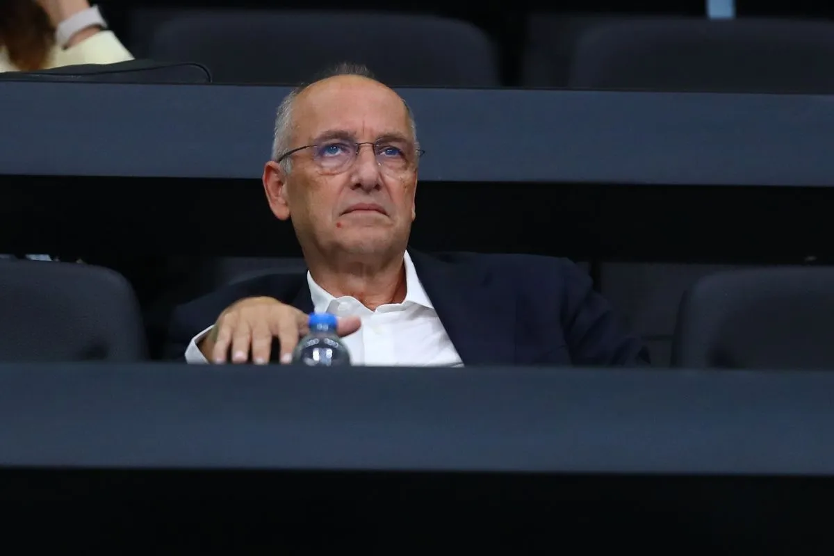 Άντρας με γυαλιά και λευκό πουκάμισο κάθεται σε αμφιθέατρο.