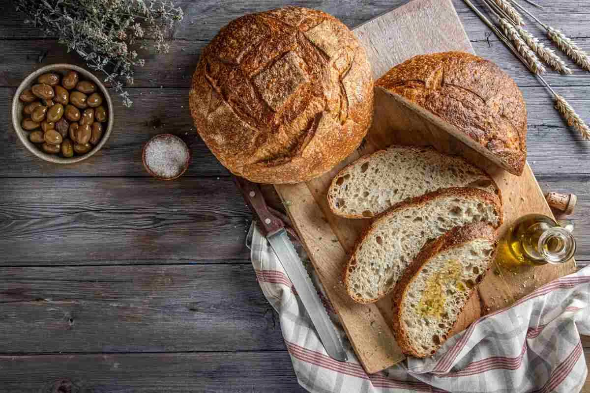 Φραντζόλες ψωμιού και κομμένες φέτες πάνω σε ξύλινη επιφάνεια μαζί με ελιές, λάδι και αλάτι.