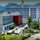 Εξωτερική άποψη πολυώροφου κτιρίου νοσοκομείου με πάρκινγκ, δέντρα και βουνά στο βάθος