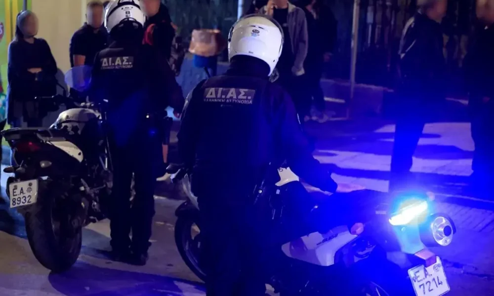 Αστυνομικοί με λευκά κράνη και υπηρεσιακές μοτοσικλέτες σε δρόμο, με αναμμένους μπλε φάρους το βράδυ