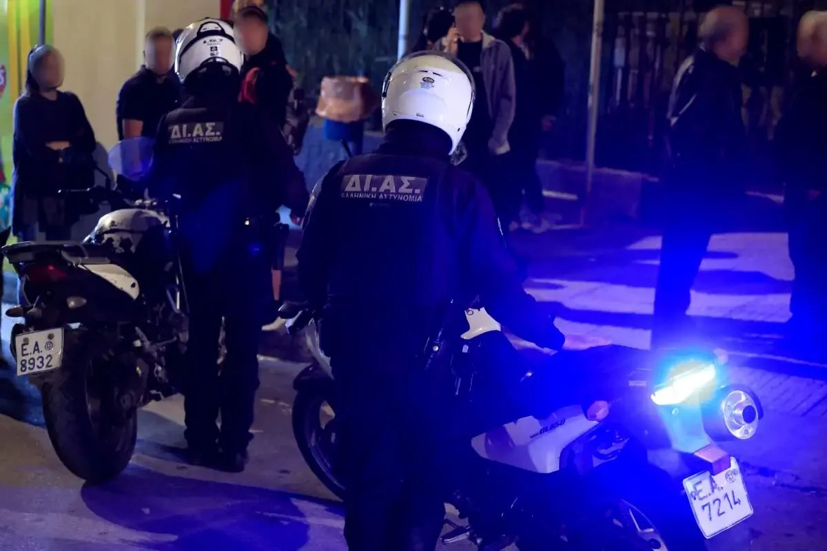 Αστυνομικοί με λευκά κράνη και υπηρεσιακές μοτοσικλέτες σε δρόμο, με αναμμένους μπλε φάρους το βράδυ