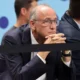 Άντρας με κοστούμι και γυαλιά κάθεται με τα χέρια σταυρωμένα
