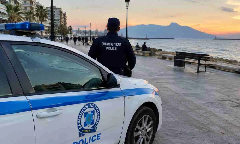 Περιπολικό της αστυνομίας σταθμευμένο σε παραλιακό πεζόδρομο την ώρα του ηλιοβασιλέματος, με αστυνομικό σε κοντινή απόσταση.