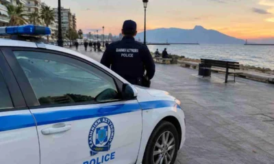 Περιπολικό της αστυνομίας σταθμευμένο σε παραλιακό πεζόδρομο την ώρα του ηλιοβασιλέματος, με αστυνομικό σε κοντινή απόσταση.