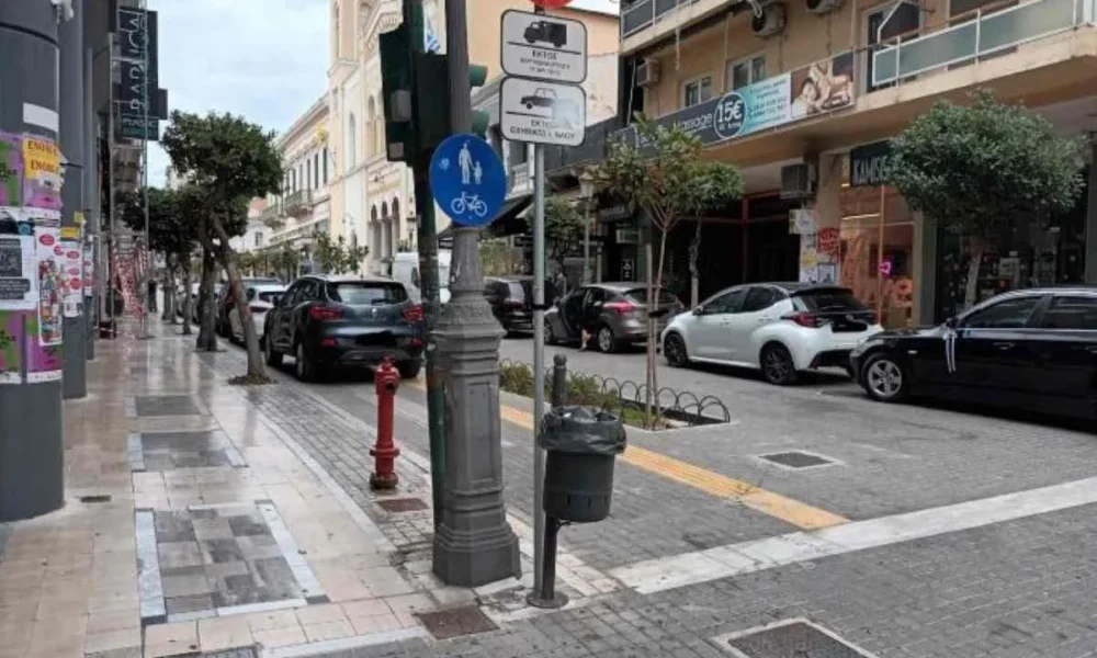 Αυτοκίνητα σταθμευμένα σε αστικό πεζόδρομο δίπλα σε πινακίδες κυκλοφορίας και κτίρια.