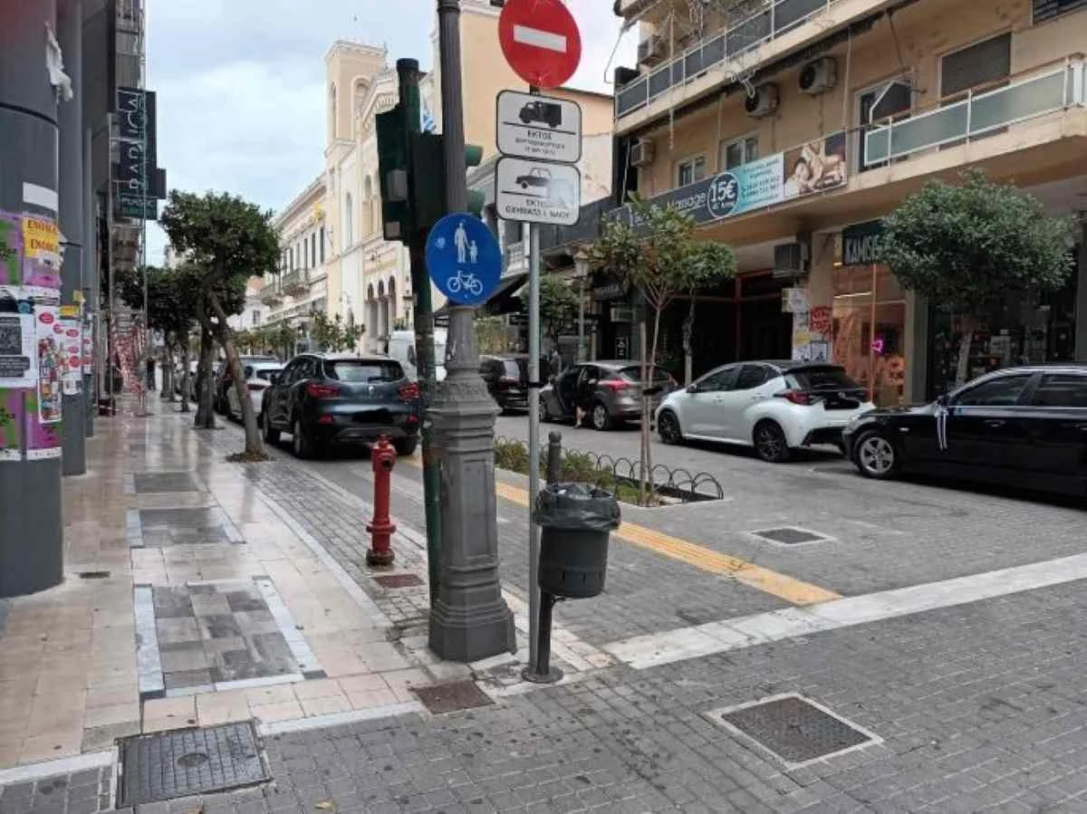 Αυτοκίνητα σταθμευμένα σε αστικό πεζόδρομο δίπλα σε πινακίδες κυκλοφορίας και κτίρια.