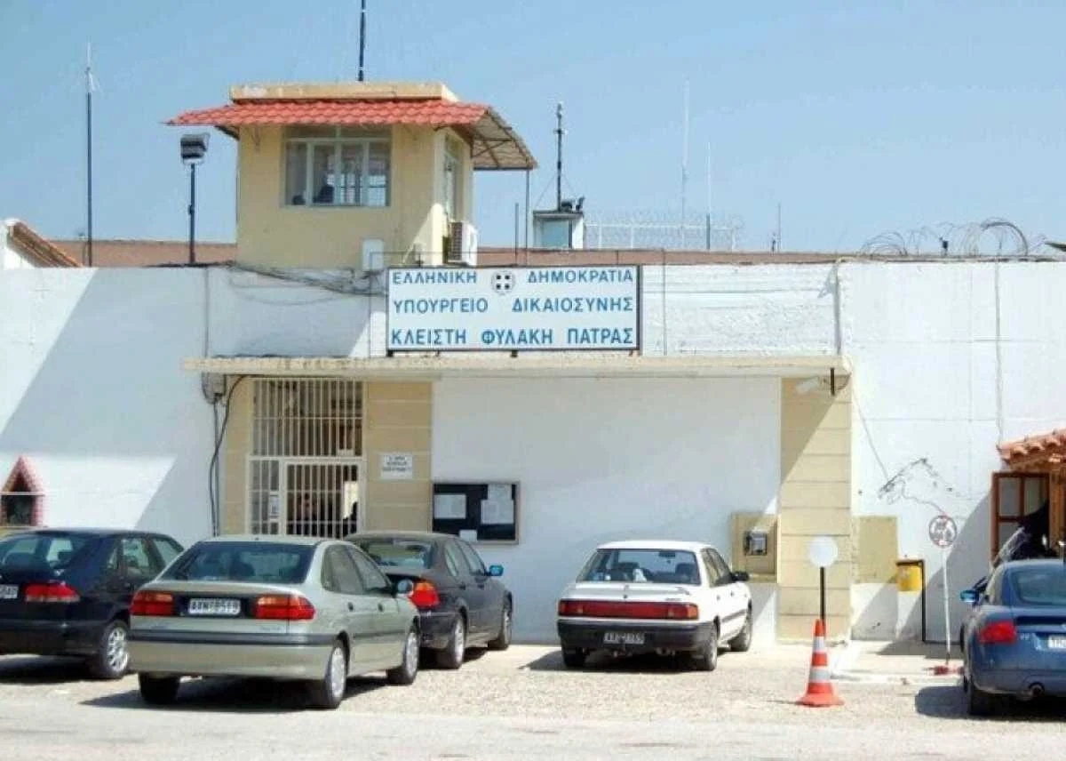 Εξωτερική άποψη κτιρίου με πινακίδα που αναγράφει Υπουργείο Δικαιοσύνης, με σταθμευμένα αυτοκίνητα μπροστά.
