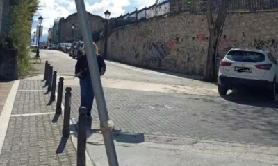 Άποψη δρόμου με πεζοδρόμιο, μεταλλικά κολωνάκια, σταθμευμένα αυτοκίνητα και ψηλό τοίχο στο πλάι.