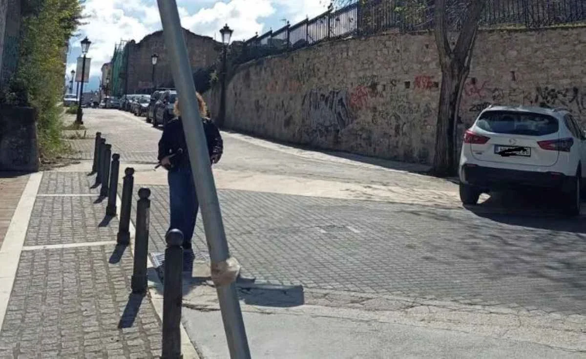 Άποψη δρόμου με πεζοδρόμιο, μεταλλικά κολωνάκια, σταθμευμένα αυτοκίνητα και ψηλό τοίχο στο πλάι.