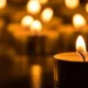 Αναμμένα κεριά σε σκοτεινό φόντο με έμφαση στο μπροστινό κερί που φλέγεται.