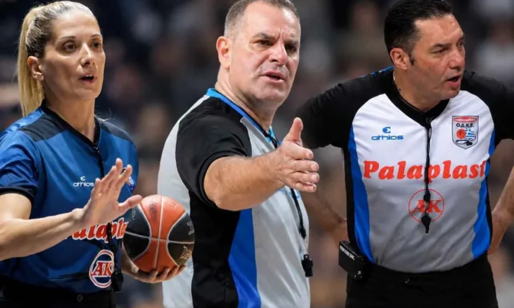 Τρεις διαιτητές μπάσκετ με αθλητικές εμφανίσεις σε αγώνα, κρατώντας μπάλα και δείχνοντας προς το παρκέ