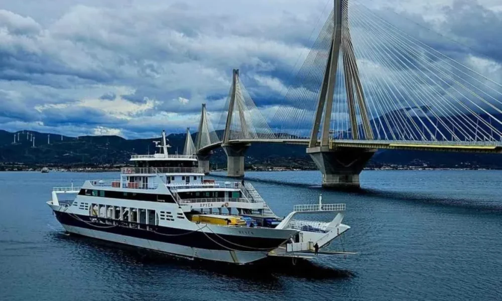 Πλοίο στη θάλασσα κάτω από μεγάλη καλωδιωτή γέφυρα με συννεφιασμένο ουρανό.