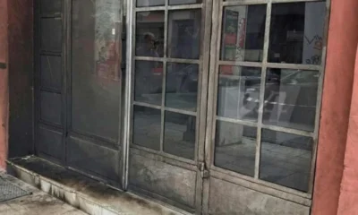 Η είσοδος καταστήματος με μεταλλική πόρτα και γυάλινα πλαίσια, με μαύρα σηγματα στην επιφάνεια του δαπέδου.