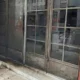Η είσοδος καταστήματος με μεταλλική πόρτα και γυάλινα πλαίσια, με μαύρα σηγματα στην επιφάνεια του δαπέδου.