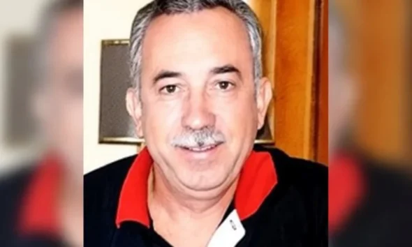 Πορτραίτο άντρα με μουστάκι και σκούρο μπλουζάκι με κόκκινο γιακά.