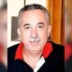 Πορτραίτο άντρα με μουστάκι και σκούρο μπλουζάκι με κόκκινο γιακά.