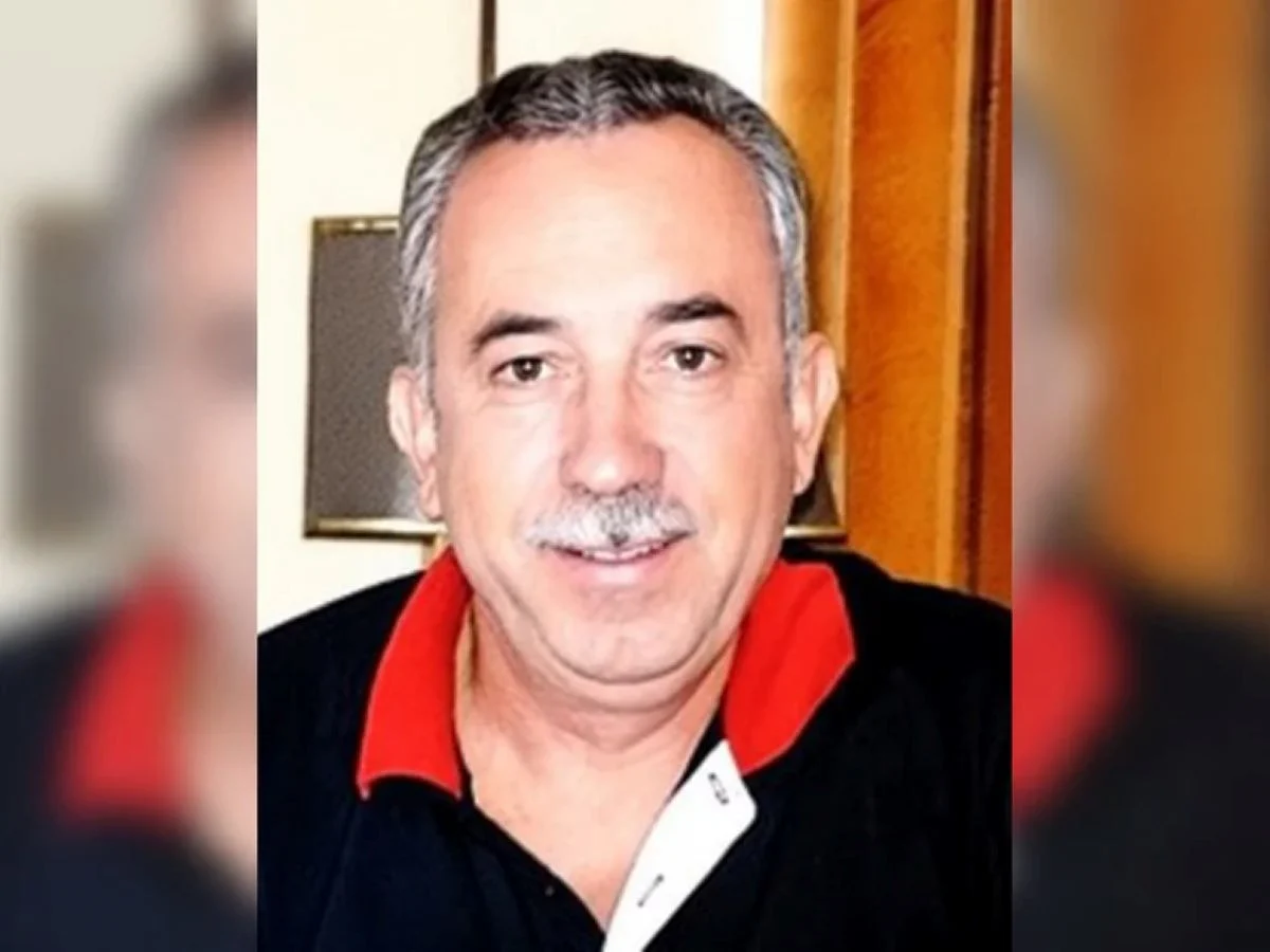 Πορτραίτο άντρα με μουστάκι και σκούρο μπλουζάκι με κόκκινο γιακά.