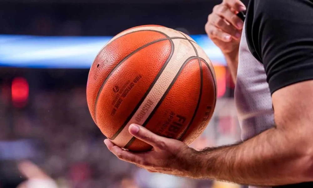Διαιτητής κρατάει μπάλα μπάσκετ με τα χέρια του μέσα σε γήπεδο