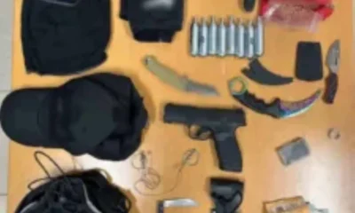 Αντικείμενα πάνω σε τραπέζι, μεταξύ των οποίων όπλο, μαχαίρια, αμπούλες, κουκούλες, σακίδιο και χαρτονομίσματα.