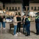 Αστυνομικοί πραγματοποιούν ελέγχους σε ομάδα νεαρών σε κεντρική πλατεία με σιντριβάνι.