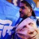 Άντρας φοράει μπλε καπέλο και κρατάει μπλε σημαία με τυπωμένο πρόσωπο.
