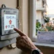 Χέρι αγγίζει ψηφιακό μετρητή ρεύματος που δείχνει κόκκινο βέλος και ποσοστό ανόδου, δίπλα σε λογαριασμό.