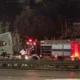 Νυχτερινή λήψη με πυροσβεστικό όχημα και άτομα κοντά σε δρόμο με πινακίδα στοπ.