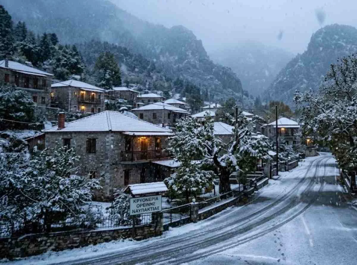 Χιονισμένο ορεινό χωριό με πέτρινα σπίτια και δρόμο καλυμμένο με χιόνι υπό χιονόπτωση.