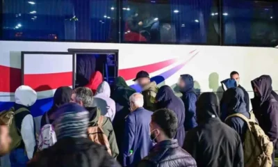 Πλήθος ατόμων με κουκούλες και σακίδια πλάτης επιβιβάζονται σε λεωφορείο