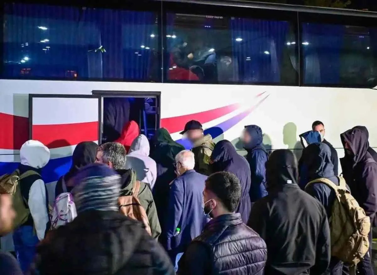 Πλήθος ατόμων με κουκούλες και σακίδια πλάτης επιβιβάζονται σε λεωφορείο
